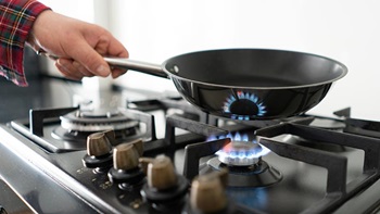 Grande plano de alguém a colocar frigideira num fogão a gás